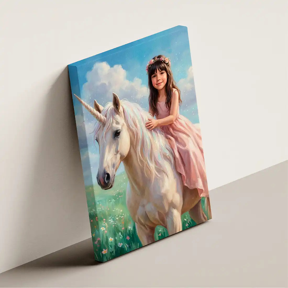 A rectangular canvas print leaning against a light gray wall, showing a painted scene of a young girl in a pink dress riding a white unicorn in a blue sky and green field.